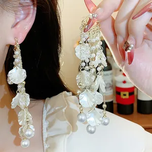 Close-up showing elegant white flower petal and pearl tassel earrings on model.