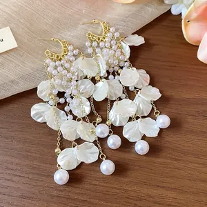 Close-up detail of elegant white petal tassel earrings with pearls on wood background