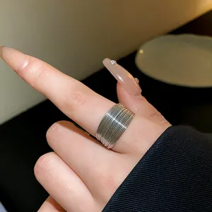 Macro detail view of a wide silver-toned multi-layered textured metal ring on a finger.