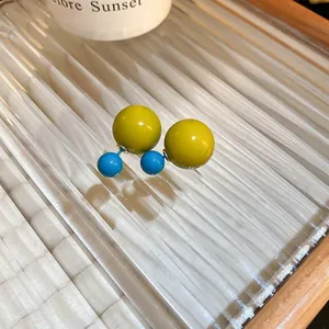 Detail view of stylish double-sided ball earrings in mustard yellow and turquoise blue.