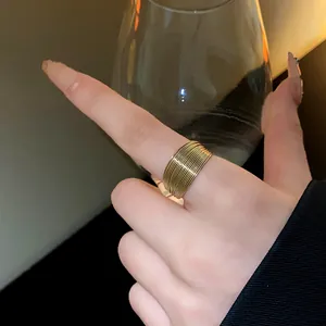 Detailed view of a wide gold multi-layered wire ring on a finger with a wine glass background