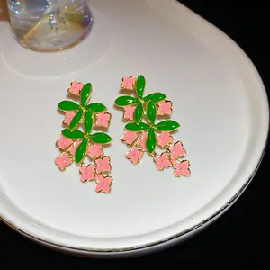 Detailed view of pink floral enamel earrings with green leaves on a white tray