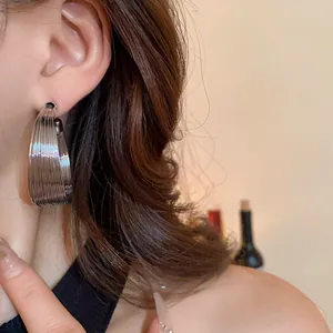 Close-up view of silver-toned textured chunky hoop earrings on an Asian model's ear.