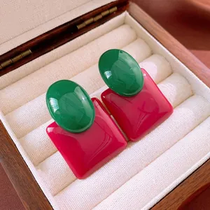 Close-up of vibrant green and pink color block enamel stud earrings in a wooden box