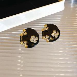 Close-up of elegant black enamel earrings with golden flower accents and rhinestones