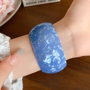 Bold iridescent blue acrylic open cuff bangle worn on wrist with elegant nail art