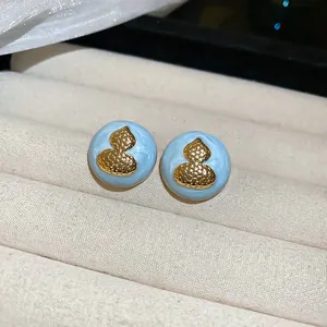 Detailed macro view of light blue enamel stud earrings featuring a golden gourd motif