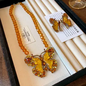 Détail d'un collier en perles de verre ambré vintage avec pendentif papillon et boucles