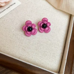 Detail view of pink enamel flower earrings with black center beads on beige fabric.