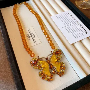 Gros plan d'un collier vintage avec pendentif papillon jaune et perles de verre orange