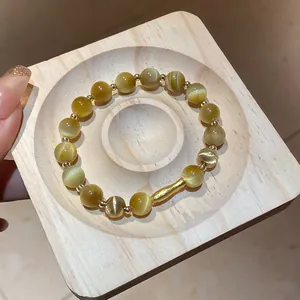 Elegante bracciale in perline occhio di gatto giallo con accenti dorati su vassoio di legno