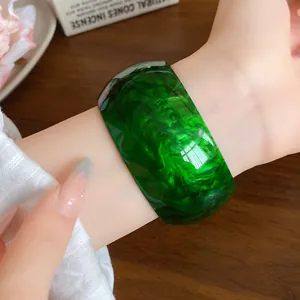 Close-up detail of a wide green marbled acrylic bangle bracelet with a stylish swirled pattern