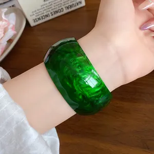 Close-up detail of a stylish dark green marbled acrylic cuff bracelet on a woman's wrist