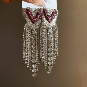 Dettaglio di orecchini a cuore in argento con strass rossi e lunghe frange di strass lucidi