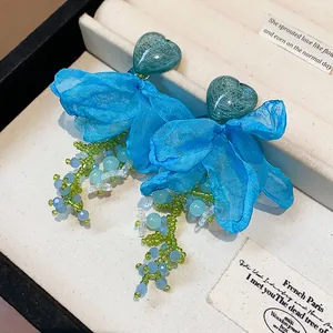 Close-up detail of blue chiffon flower tassel earrings with blue heart shaped studs
