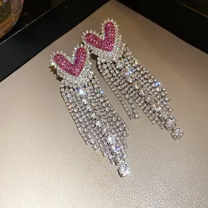 Dettaglio ravvicinato di orecchini a cuore con lunghe nappe di cristallo scintillante.