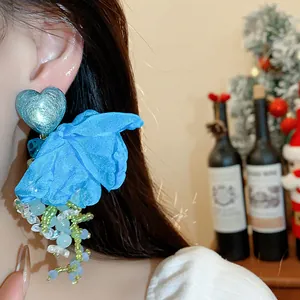 Detail view of blue chiffon flower earring with heart stud and beaded tassels on a model ear.