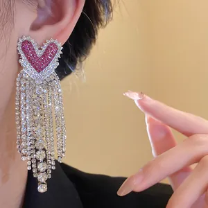 Dettaglio di orecchini a cuore con lunghe nappe di strass e pietre rosa