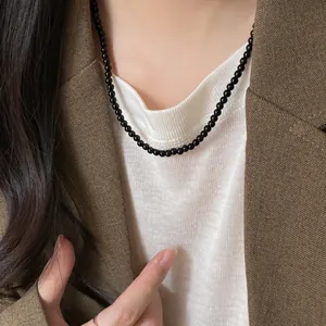 Detail shot of a minimalist black bead necklace worn over a white top and brown blazer.