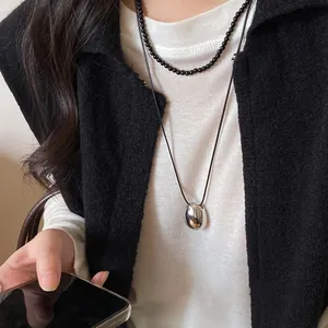 Detail of a minimalist silver oval pendant on a black leather cord sweater chain.