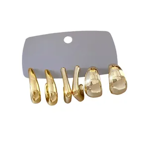 Set of three irregular gold geometric hoop and stud earrings on a grey display card.