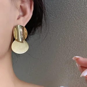 A detailed close-up of gold-colored round brushed metal stud earrings on a model