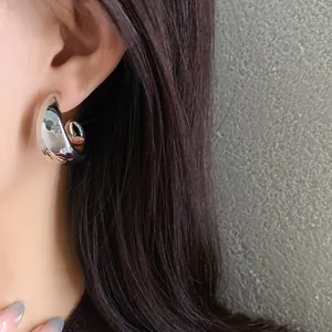 Detail view of a silver minimalist irregular geometric C-shaped earring worn on a model's ear
