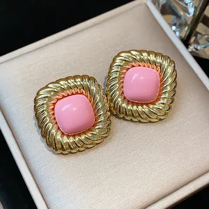 Close-up of vintage twisted gold square stud earrings with a smooth pink center detail.