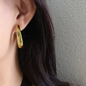 Close-up of minimalist gold irregular teardrop earring worn on ear with dark hair
