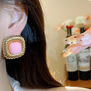 Close-up of distorted square gold pleated stud earring with pink center on ear