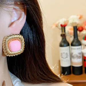 Detailed view of stylish gold twisted square stud earrings with a pink center on an ear