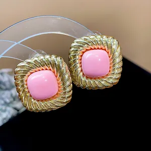 Close-up detail of stylish twisted square earrings with gold pleated frame and pink center