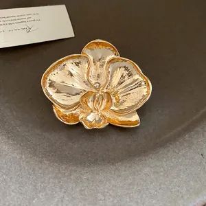 Macro detail of a vintage gold-toned orchid flower brooch with textured petals.