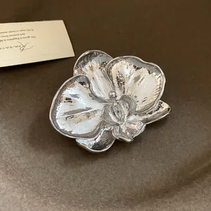 Close-up detail of a vintage silver orchid flower brooch on a brown felt background