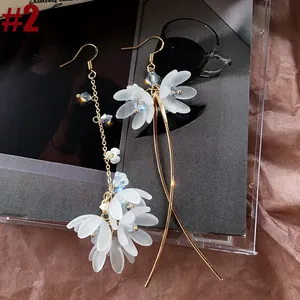 Close-up of asymmetrical long tassel earrings with frosted white floral petals and blue beads.
