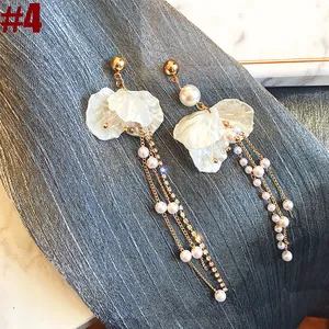 Detail of long pearl tassel earrings with delicate white flower petals on gray fabric.