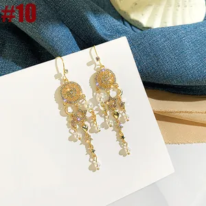 Detail of gold-tone long tassel earrings with pearls and starry charms.