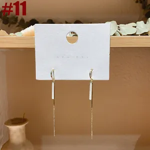 Close-up of long gold tassel earrings with pearl accents on a branded display card.