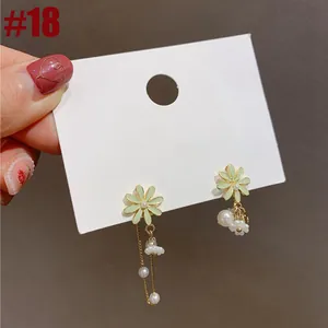 Macro view of daisy flower earrings with dangling pearl tassels on a white display card