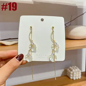 Detail showing elegant long tassel earrings with white shell petals and gold chains