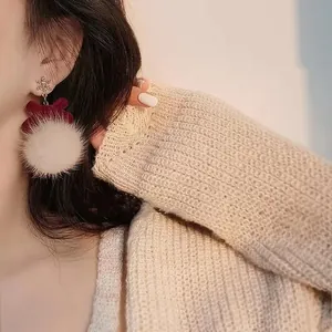 Primer plano detallado de elegantes pendientes navideños con pompón blanco y lazo rojo en modelo