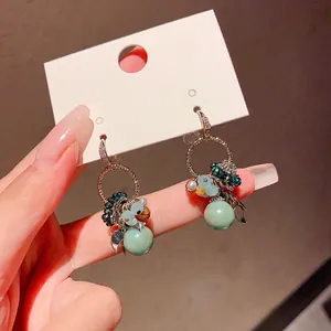 Close-up of Bohemian zircon earrings with green glass beads and delicate charms.