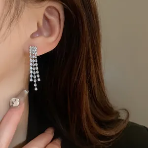 Close-up of elegant silver tassel earrings with sparkling rhinestones on model's ear