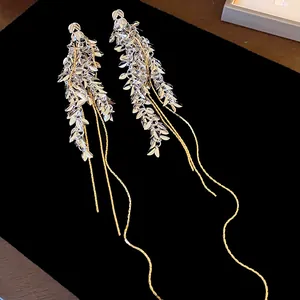 Detailansicht langer Quastenohrringe mit silbernen Blatt- und Ähren-Designelementen.