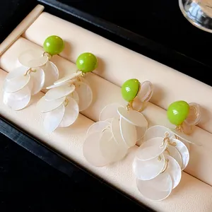Detail view of green bead earrings with white shell tassels in stud and clip-on styles