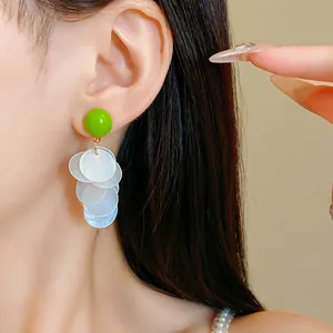 Close-up of green round stud with white tiered shell tassels earring on model ear