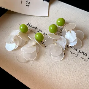Close-up of elegant shell tassel earrings with green bead accents and silver needle studs.