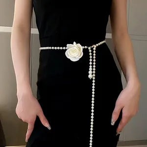 Elegant detail view of a long pearl necklace featuring a white rose worn as a waist chain
