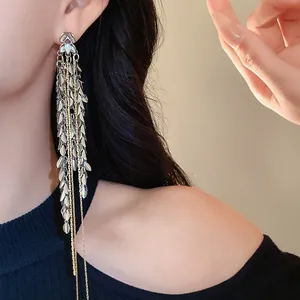 Detailaufnahme eleganter Quastenohrringe mit Blatt- und Weizenmotiv an einem Modell.