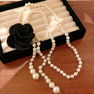 Macro detail of a long vintage pearl necklace featuring a large black camellia rose charm
